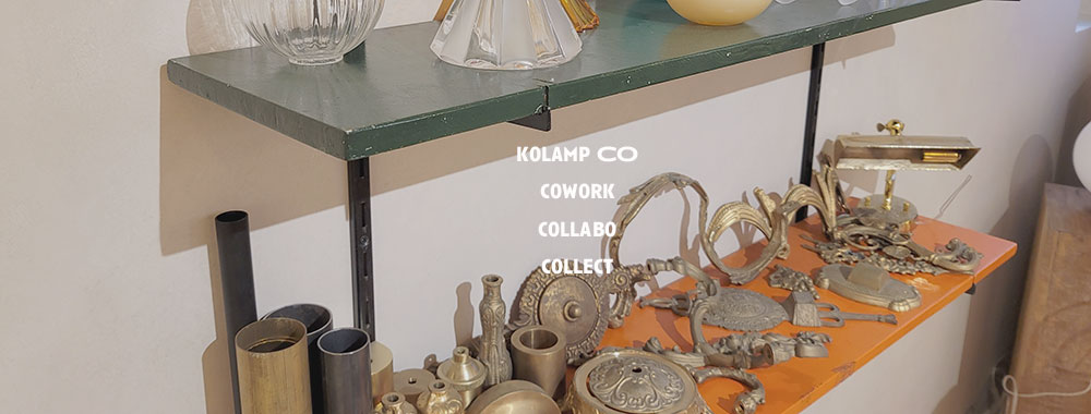 코램프의 브랜드 슬로건인 COWORK, COLLABO, COLLECT 가 배치된 인테리어 공간. 창으로 들어오는 자연광과 벽면 선반에 전시된 빈티지조명과 샹들리에조명이 아늑한 분위기를 더하며, 카페조명을 연상시키는 디자인이 돋보임.